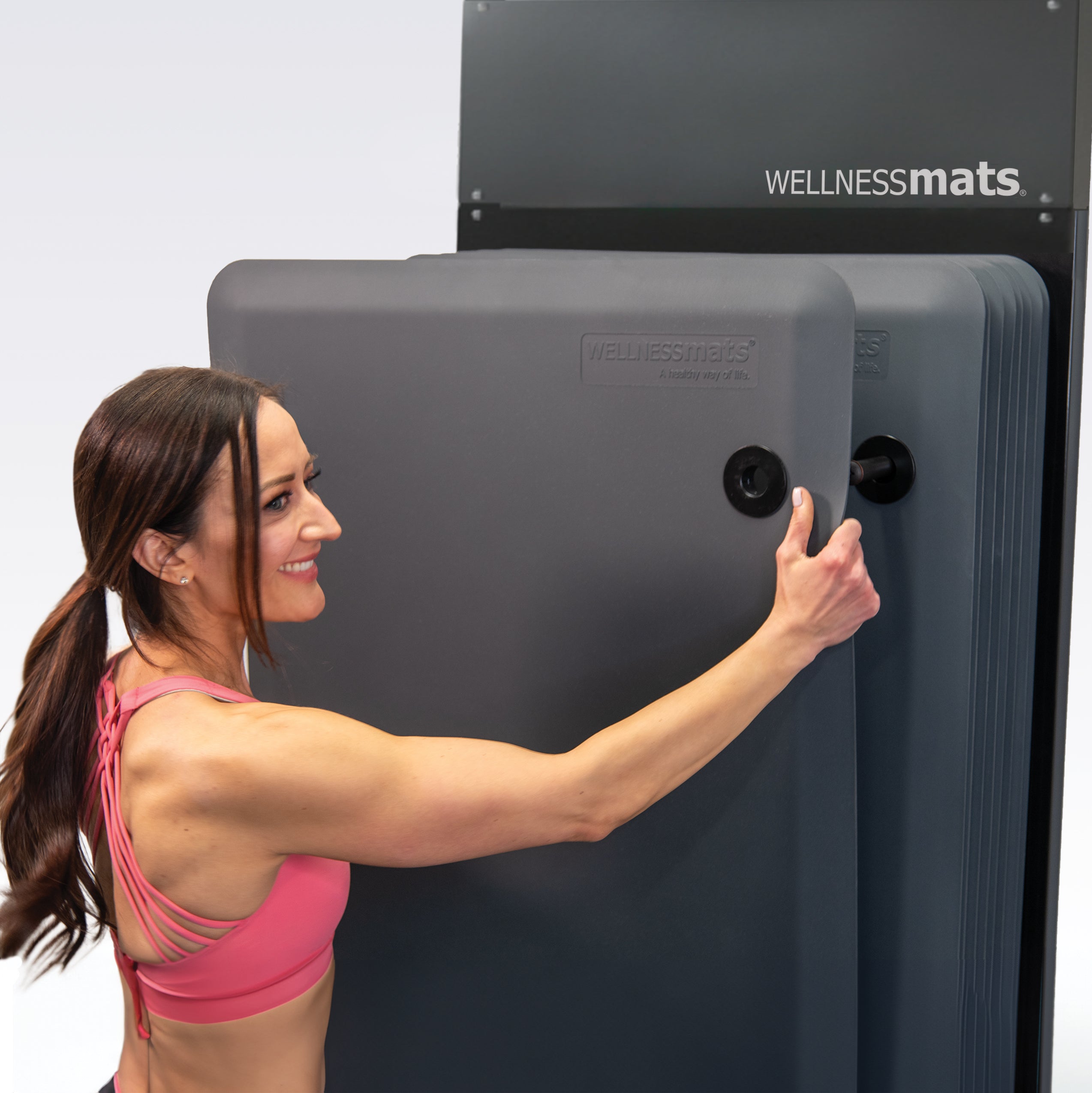 Woman removing FitnessMat from wall rack.