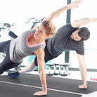 A man and a woman each doing a yoga pose on a gray FitnessMat