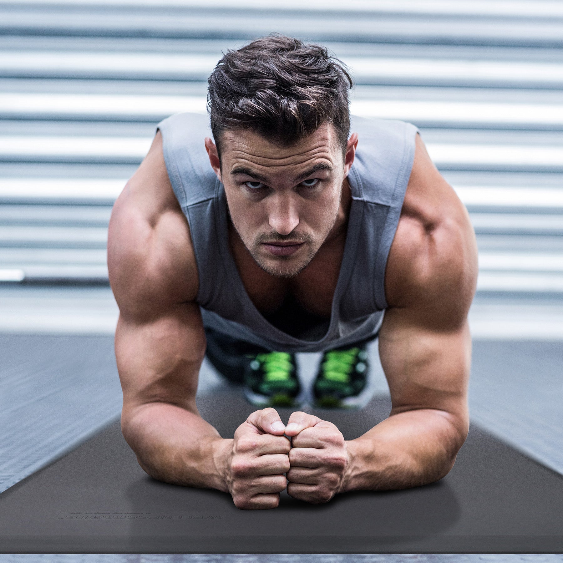 A man facing camera doing a plank pose on a gray FitnessMat