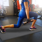 A woman in a gym holding dumbells and doing lunges on a gray FitnessMat.