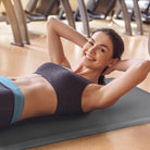 A smiling woman doing crunches at a gym on a gray FitnessMat.
